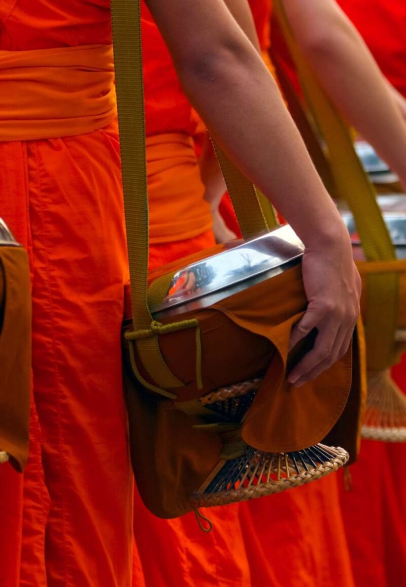 Buddhist monks in orange robes holding alms bowls during luxury Southeast Asia tours.