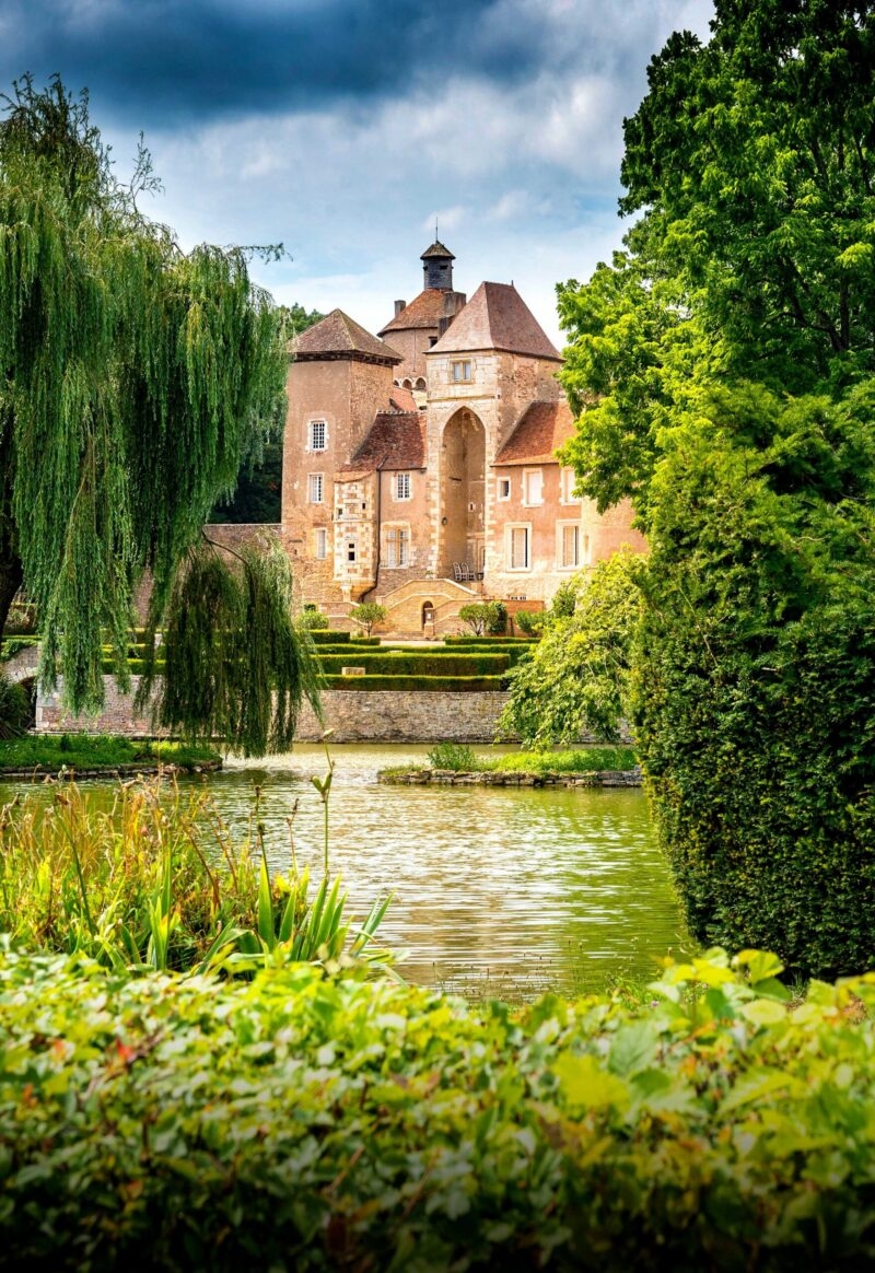 A beautiful historic chateau building in France, with a lake out front with willow trees around the edge