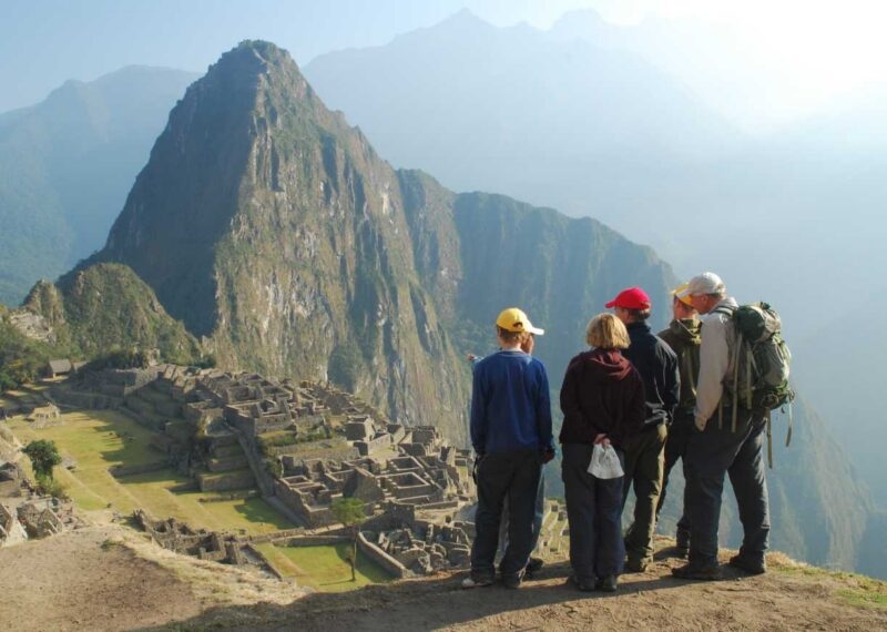 A group of five people wearing hiking gear stands on a high viewpoint overlooking the vast ruins of Machu Picchu and a massive mountain, ideal for luxury Machu Picchu trips.
