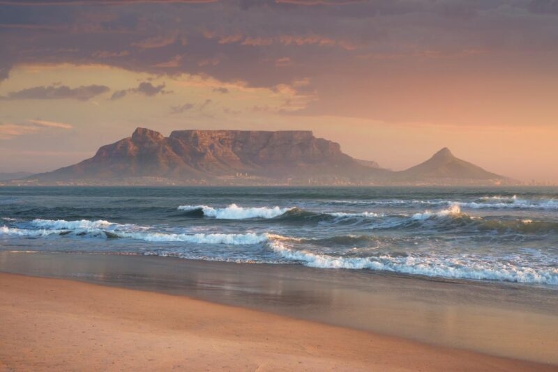 Rolling waves of Sunset Beach near Cape Town with a view of Table Mountain in the background at dusk on a luxury Africa trip