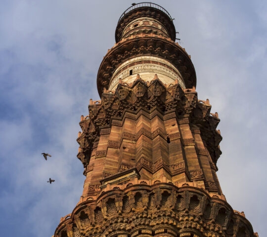 Qutb Tower in India shot from below, capturing birds in the cloudy sky