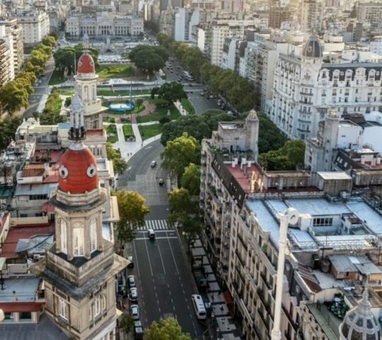 High-angle view of a city with a central domed palace and park during a bright orange sunset.