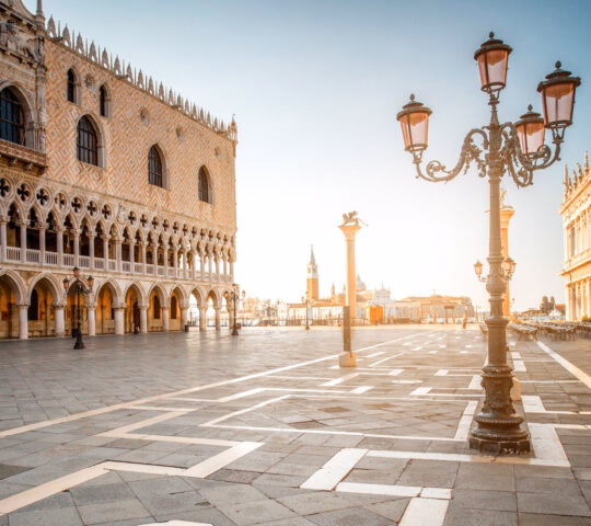 View of the Doge's Palace and an ornate black street lamp in a sunlit square in Venice, Italy.