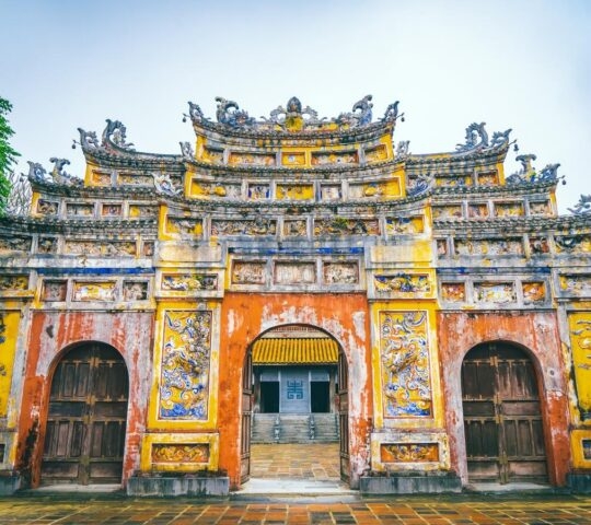Ornate yellow and red stone gate with three arched entrances and detailed roof carvings at a historic site.