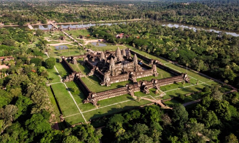 Aerial view of a large, ancient stone temple complex surrounded by lush green forests and clearings.