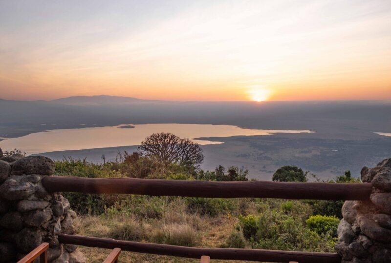 A luxury Ngorongoro Crater safari sunset viewed from a stone lodge balcony overlooking the lake and distant mountains.