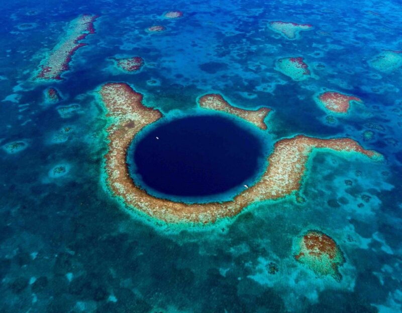 Aerial view of a large circular deep blue marine sinkhole surrounded by a shallow turquoise coral reef.