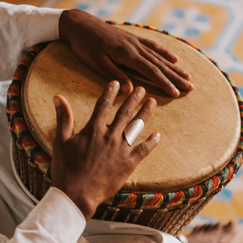 A person's hands rest on the surface of a traditional drum with a colorful rim.