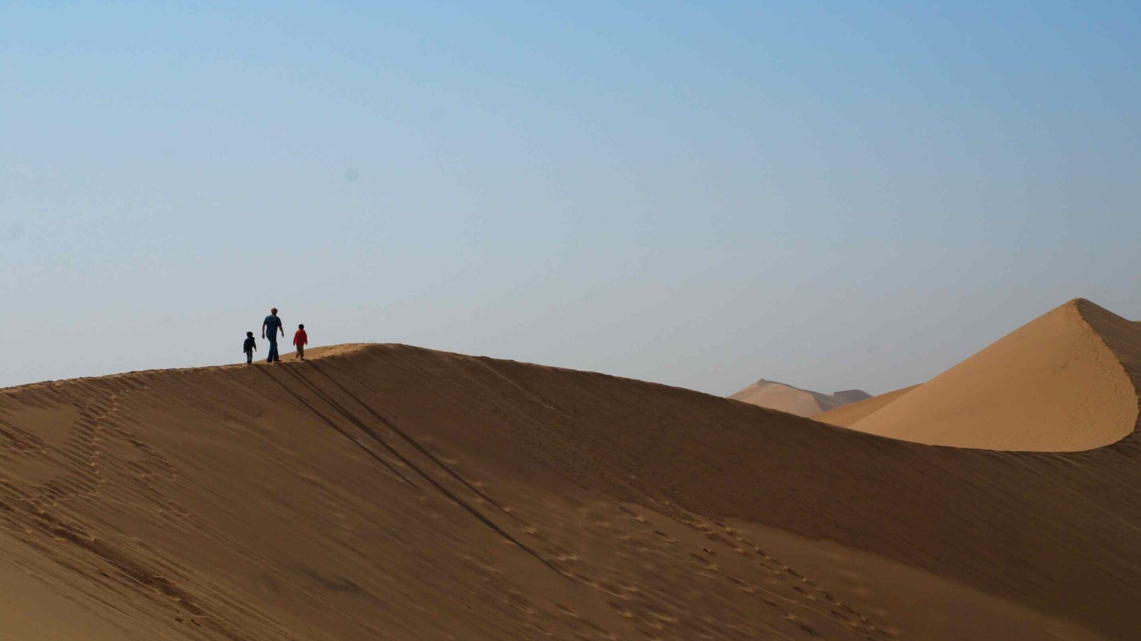 Silhouette of three figures walking on the crest of a high sand dune in the desert.