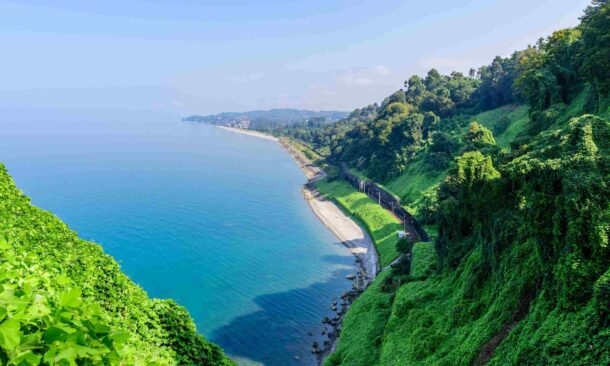 A scenic view of steep green hills overlooking a calm blue ocean and a narrow sandy beach strip
