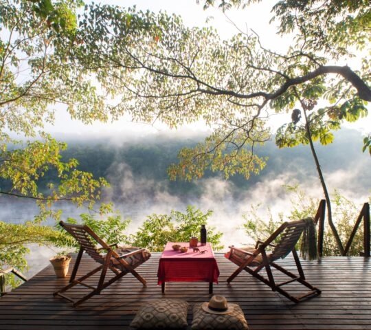 Two chairs on an outdoor deck overlooking a mist-shrouded river.