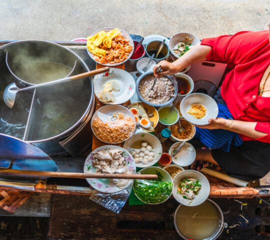 Top view old woman cooking Thai noodle soup Tom Yam style on Thai tradition boat in local floating market, Famous traditional Thai street food for tourists