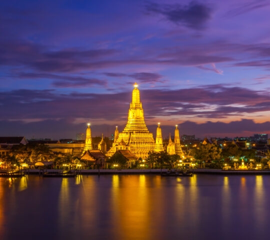 Bangkok's Wat Arun temple at night, glowing golden against a purple sky