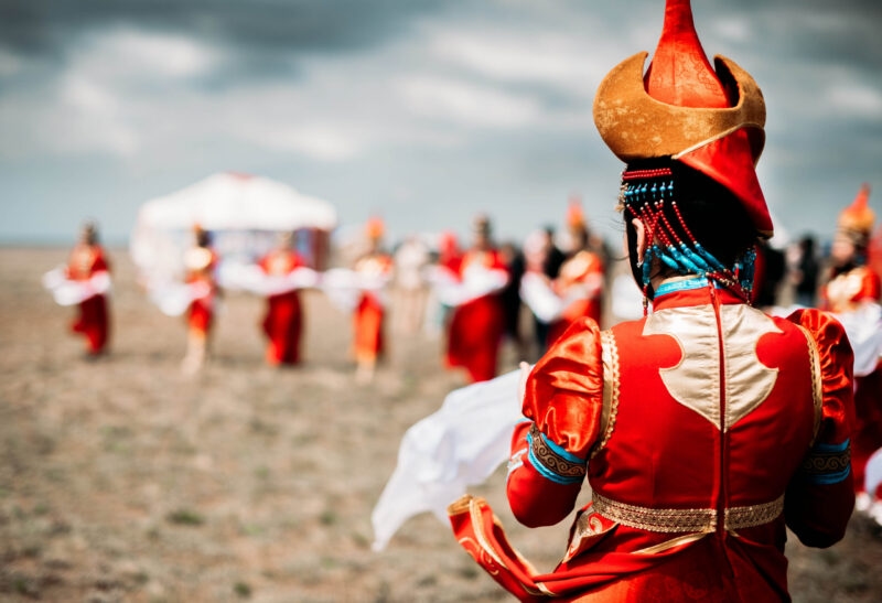 A person in a red and gold traditional costume in an open field during luxury Mongolia vacations.