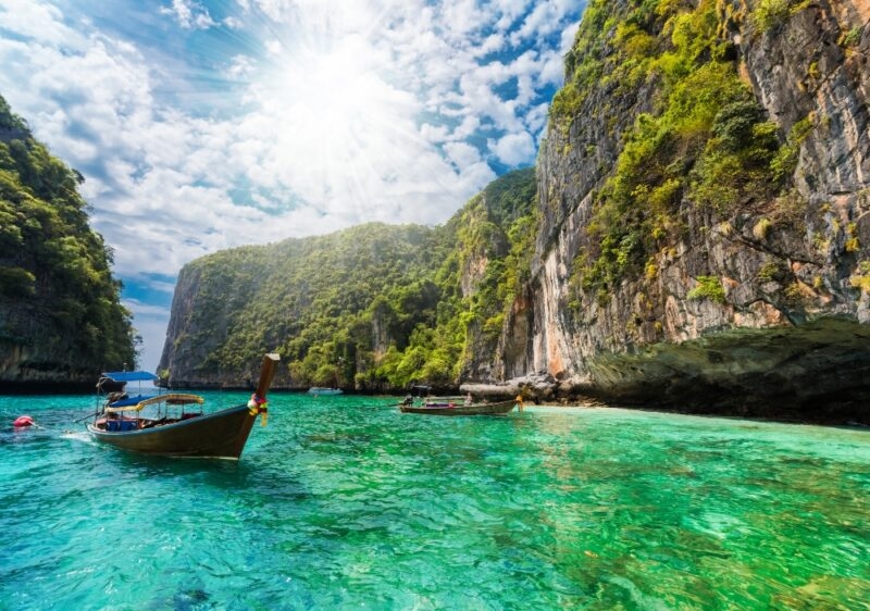 Longtail boats on turquoise water by limestone cliffs in Thailand during luxury Asia grand tour vacations.