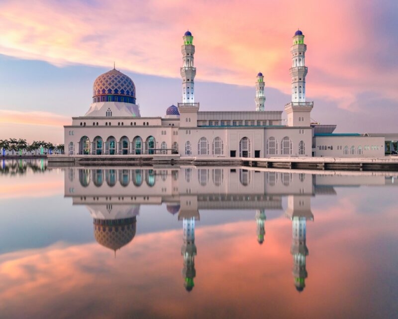 A grand white mosque with minarets reflected in still water at sunset during luxury Asia grand tours.