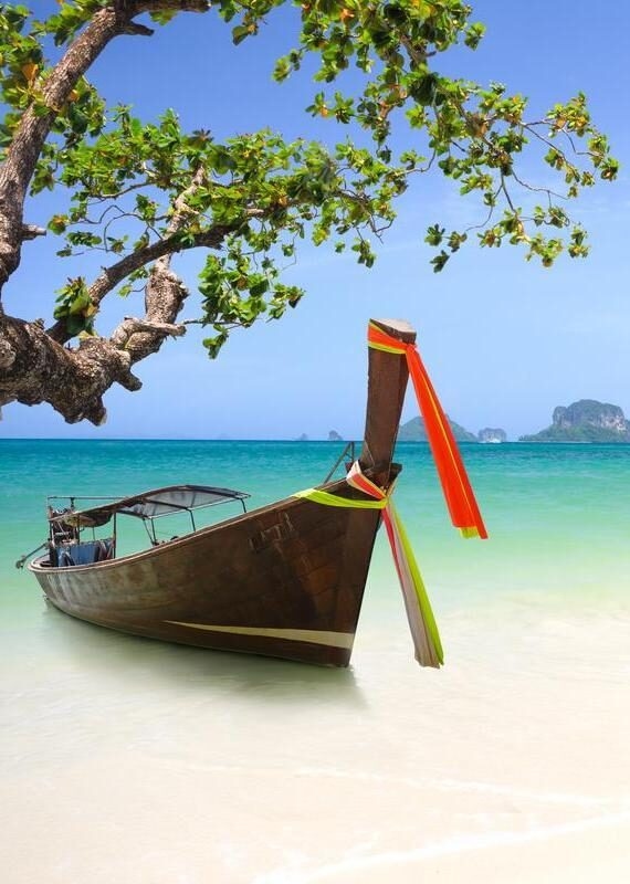 Traditional wooden longtail boat moored on a white sand beach with turquoise water and islands in the distance.