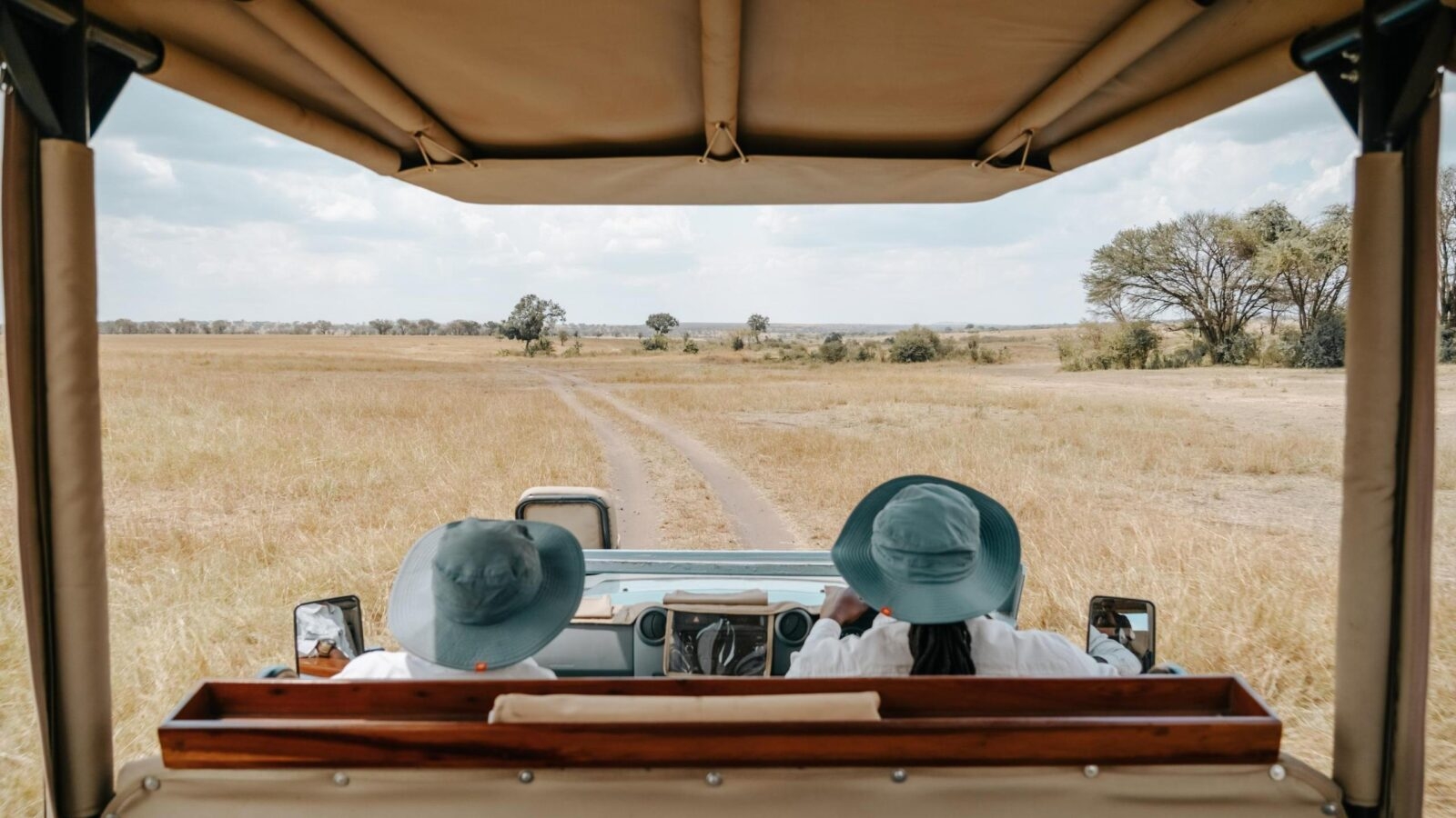 Two people in a safari vehicle looking out at a grassy savannah.
