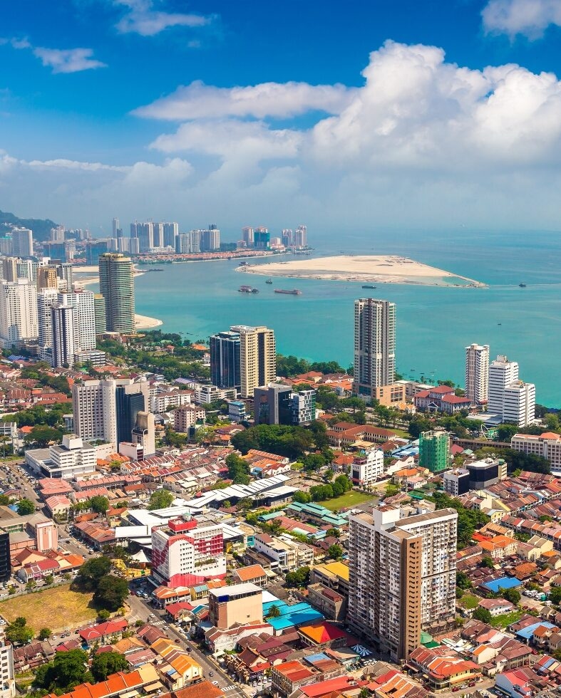 High-rise buildings line the coast of Penang under a blue sky during luxury Malaysia vacations.