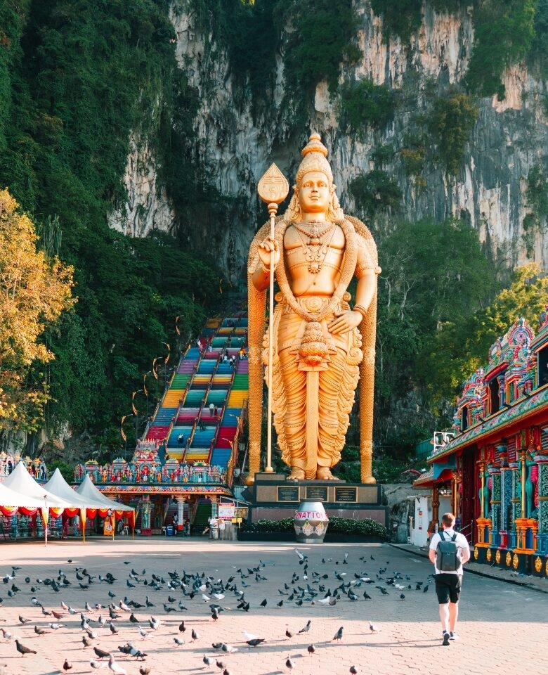 A person walks towards a large golden statue next to colorful stairs and pigeons on the ground.