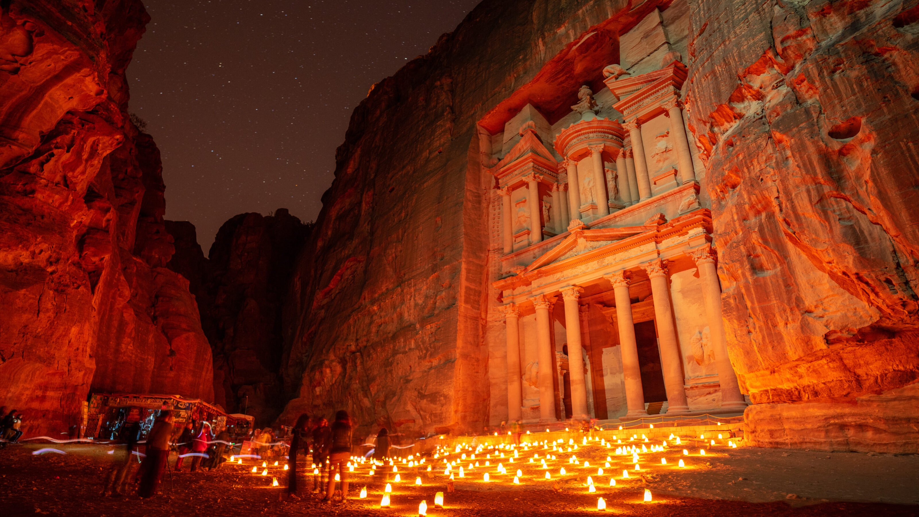 Night view of Al-Khazneh in Petra with candles and starry sky.