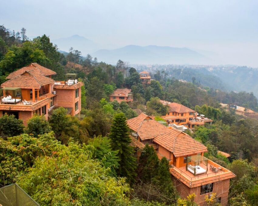 Terracotta-roofed villas on a hilly forest with misty mountains in the background.