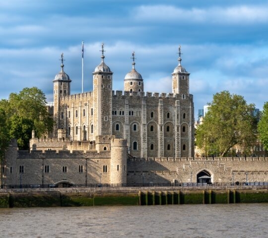 Historic stone fortress with towers by a river under a cloudy sky.