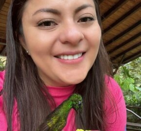 Person in pink shirt holding a hummingbird feeding from a red feeder.
