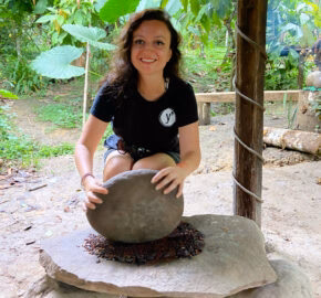 Person in a black shirt grinding something on a stone in a lush green setting.