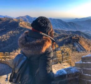 Person gazing at the Great Wall of China winding through mountains at sunset.