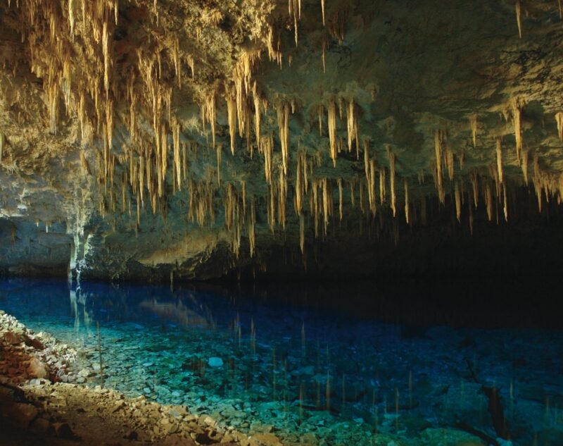 Interior of a cave with many stalactites hanging over clear blue water on luxury Pantanal vacations.