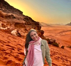 Person in desert with rocky formations and sunset in the background.
