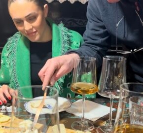 People enjoying wine and cheese at a table with a painting in the background.