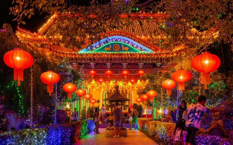 Traditional Chinese architecture adorned with bright lights and red lanterns at nighttime, with visitors strolling.