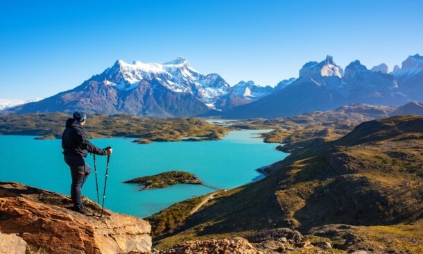 Hiker overlooking a turquoise lake and mountain range.