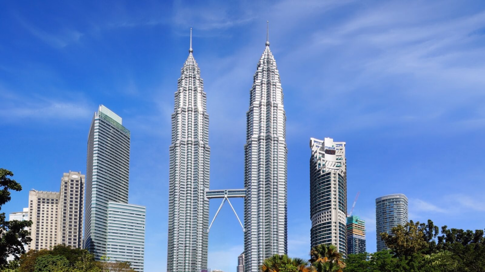 Twin skyscrapers towering above trees against a clear blue sky.