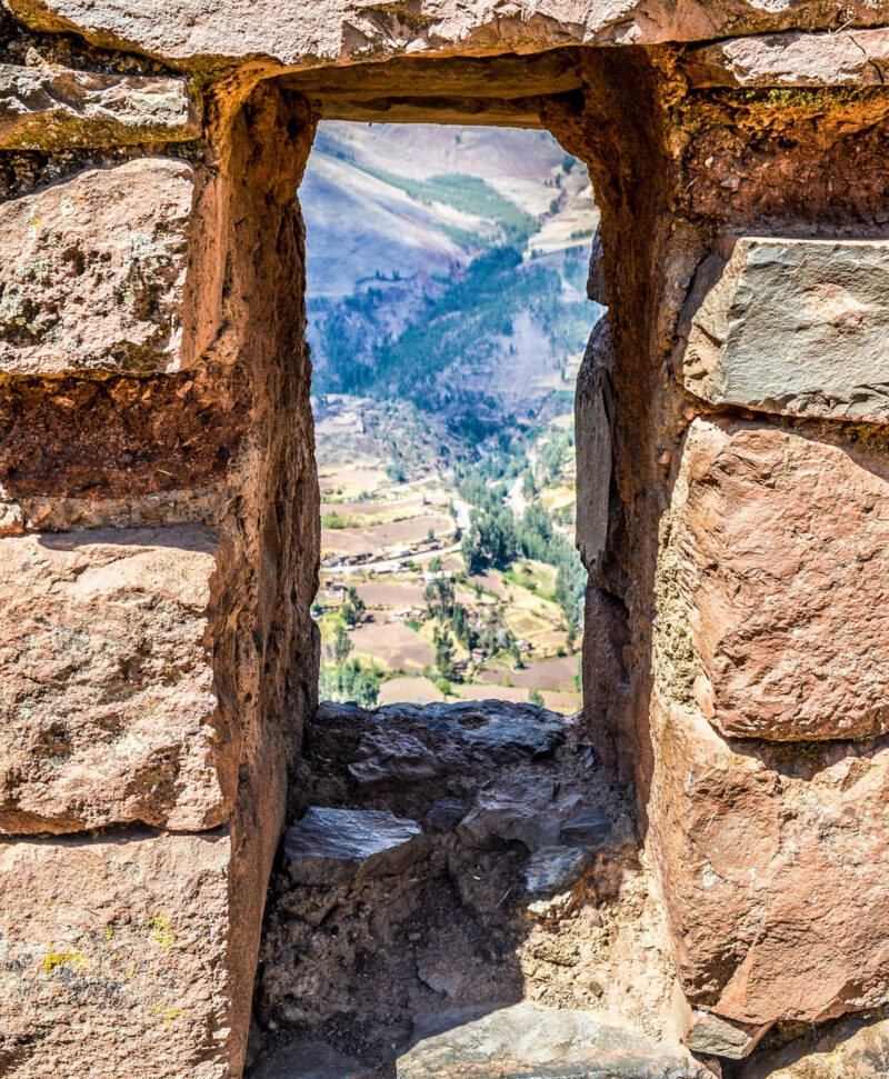 A scenic valley viewed through an ancient stone window with clear blue skies above.
