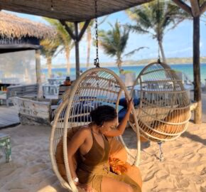 Person in a beach swing chair with palm trees and the ocean in the background.