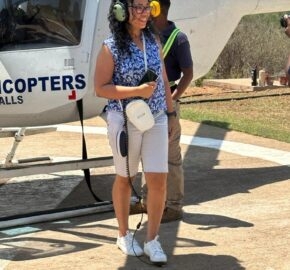 Person in headset stands by a helicopter, with another individual in the background.