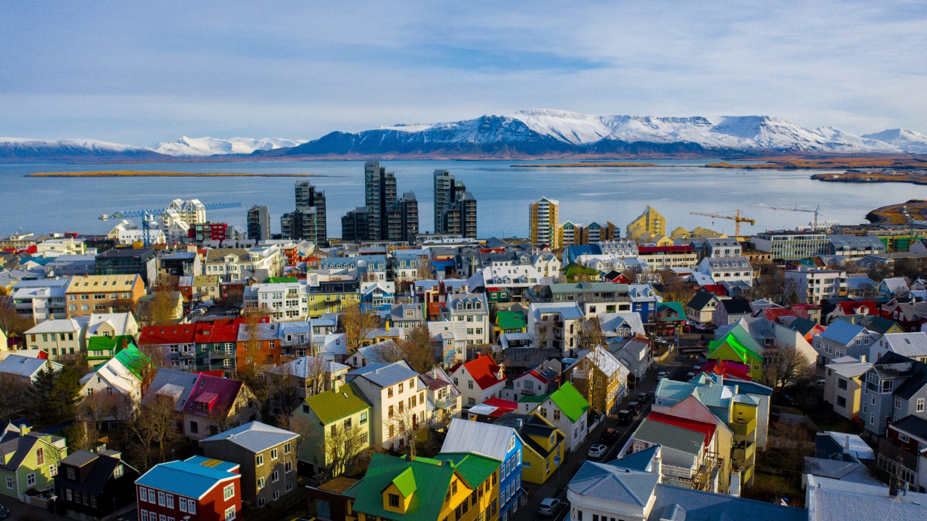 An aerial view of a colorful cityscape with a mountainous backdrop and a blue bay.