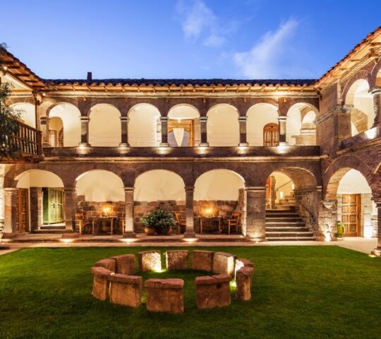 Elegant courtyard at twilight with arches, balcony, and lit interior rooms.