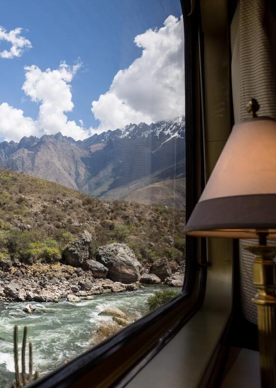 Luxury Peru Tours - View from a train window overlooking a river and rugged mountains with a lamp in the foreground.