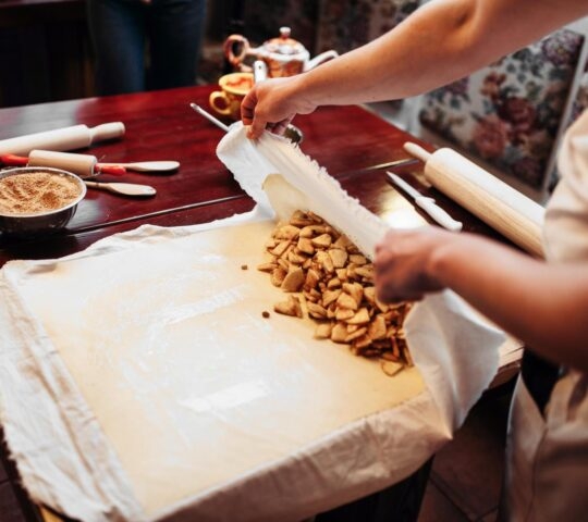 Person preparing dough with a pile of apple pieces on the side for baking.