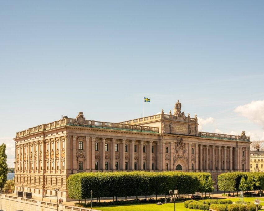 A classical building with Swedish flags under a clear sky.