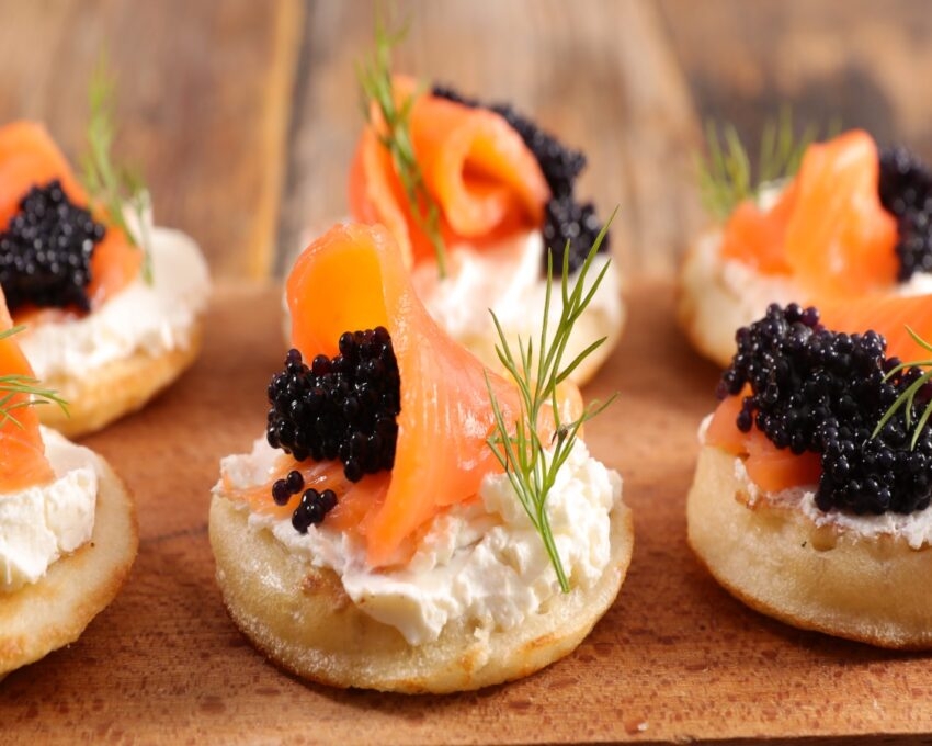 Appetising canapés with smoked salmon, cream cheese, caviar, and dill on a wooden surface.