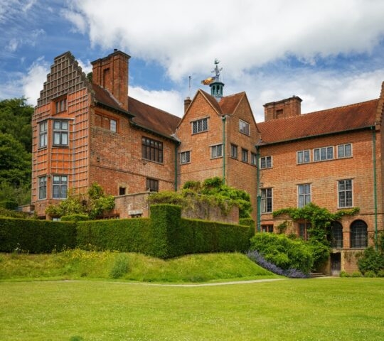 Traditional brick country house with distinctive chimneys and a manicured lawn.