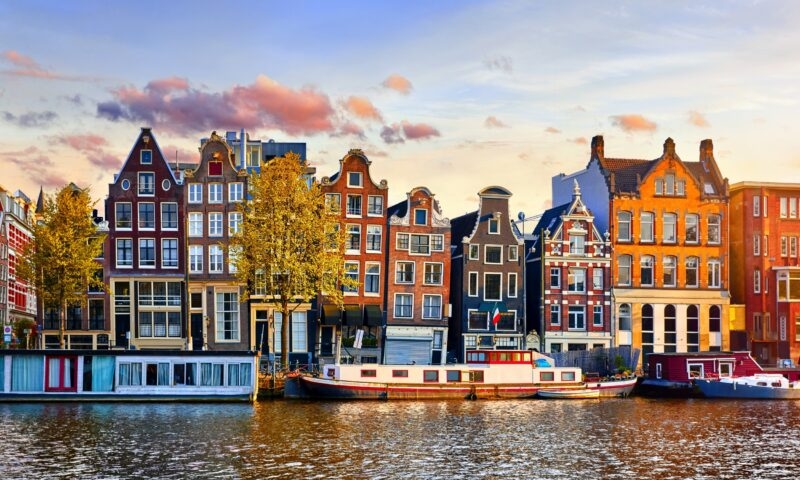 Colourful Dutch houses by a canal at sunset with a houseboat in Amsterdam.