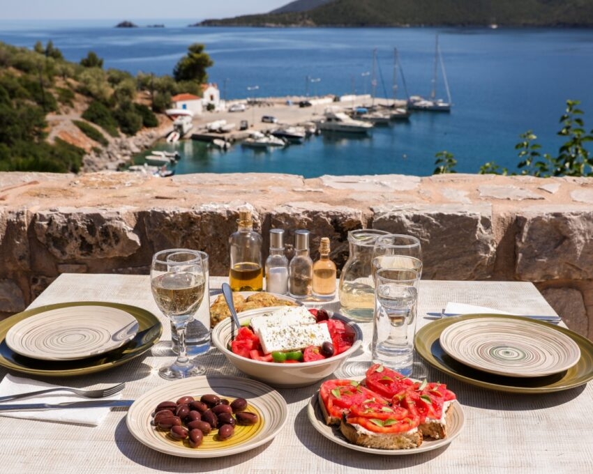 Table with Mediterranean food overlooking a seaside with boats.