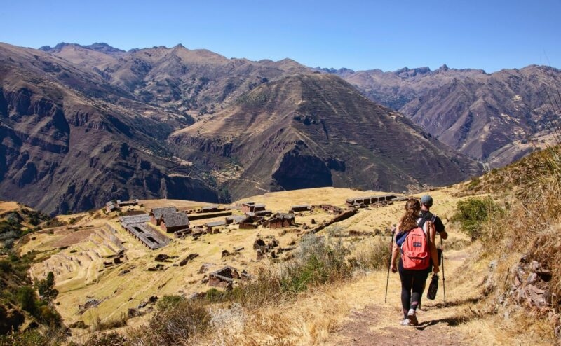 Two hikers descending a hill toward ancient ruins in a mountain valley during luxury Inca Trail trips.