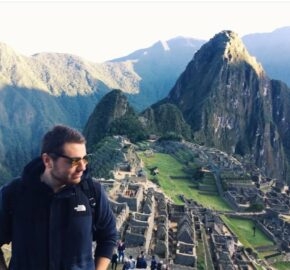 Person in a jacket standing before ancient Machu Picchu ruins amidst green mountains.